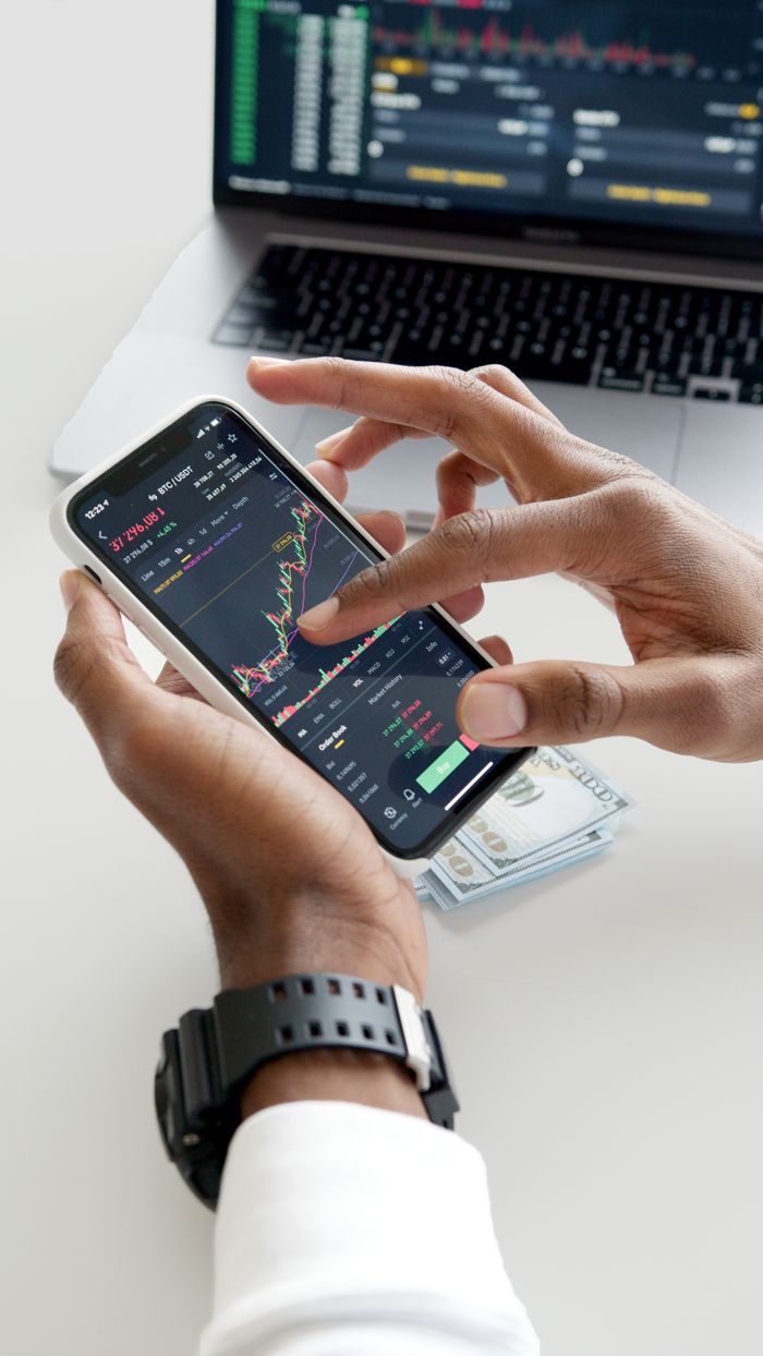 creative-03 Hands using smartphone trading app with charts, dollar bills in background.