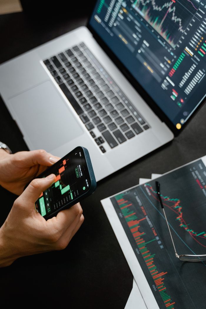 brand-01 Hands holding phone with financial graph, laptop in view.