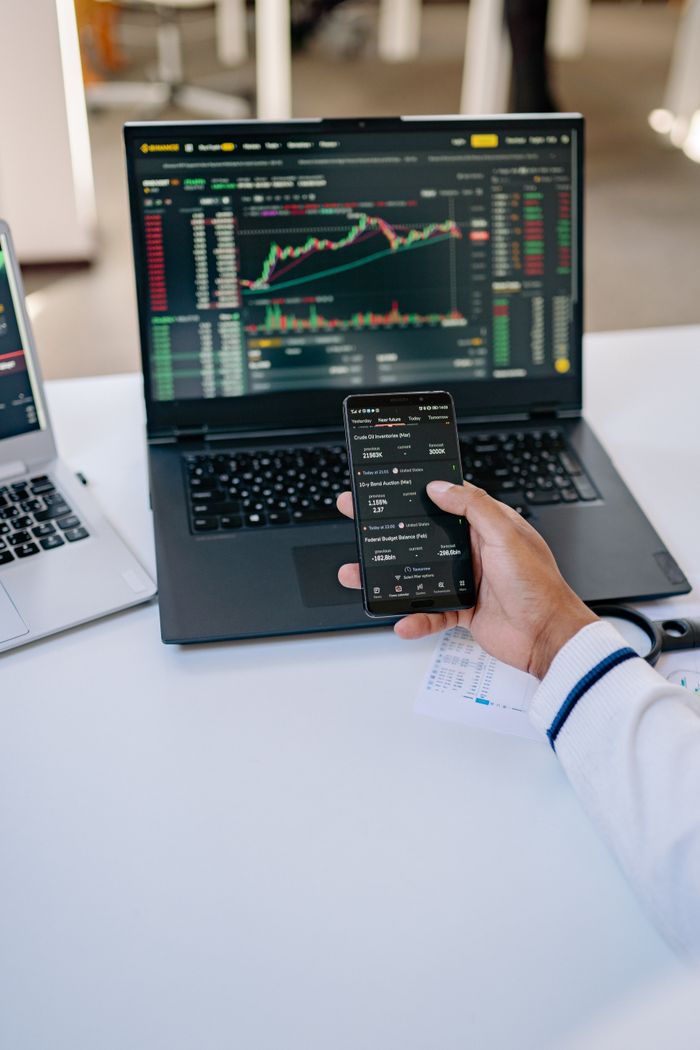 mobile-02 Person analyzing stock market data on a laptop and smartphone at a desk.